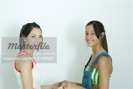 Deux jeunes amis femmes main dans la main, côté vue, souriant à la caméra, portrait