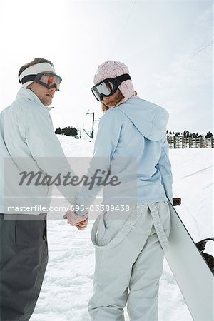 Deux jeunes amis marchant, holding hands, regarder par-dessus les épaules, un snowboard comptable, vue arrière