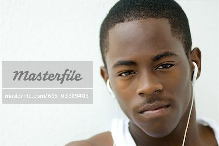 Teenage boy listening to earphones, looking at camera, portrait