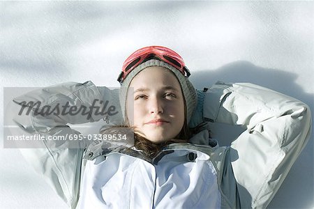 Teen girl lying on snow with hands behind head, head and shoulders