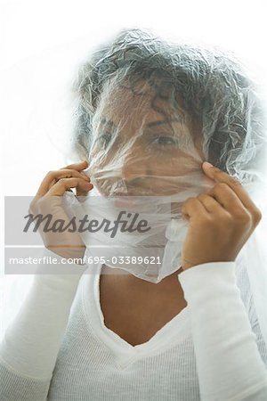 Woman holding plastic bag over head, looking at camera