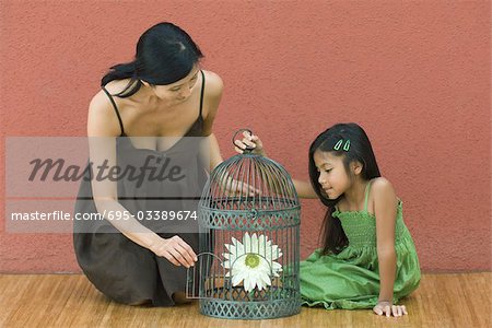 Woman and girl with birdcage containing flower, woman opening door