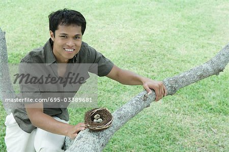 Homme assis dans l'arbre à côté du nid d'oiseau