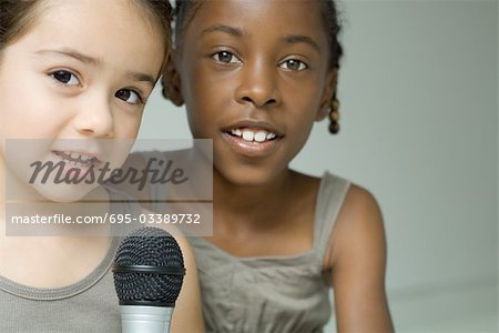 Two young girls singing into microphone together, both looking at camera