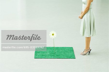 Woman standing by square of artificial turf with fake flower, chest down