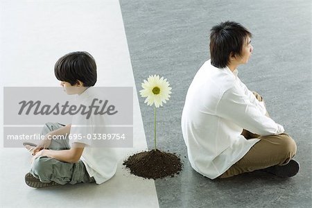 Boy and man sitting back to back, a single flower between them