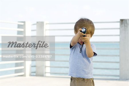 Little boy standing outdoors, holding a flashlight in front of his face