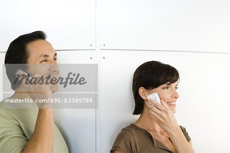 Homme et femme à l'aide de téléphones cellulaires, à la recherche de suite, souriant