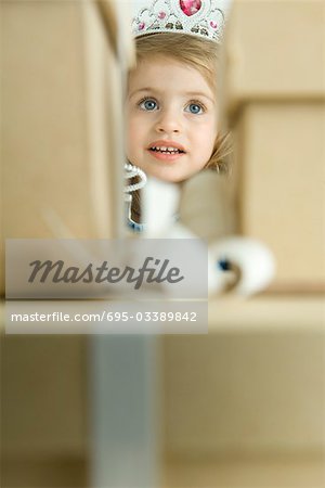 Girl dressed as a princess, peering through stack of gifts