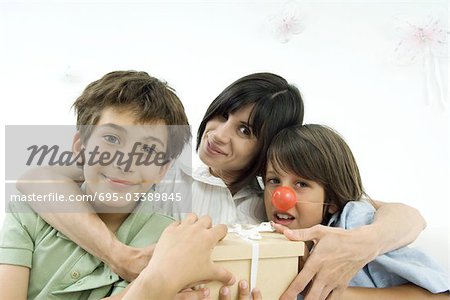 Mother with arms around her two sons, one wearing clown's nose, portrait
