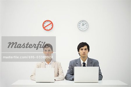 Des employés de bureau assis au-dessous des horloges, à l'aide d'ordinateurs portables, avertissement céder une horloge