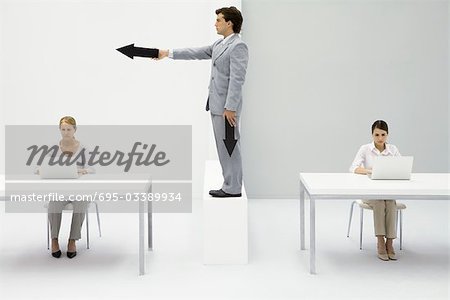 Professional women working in office, man standing between them, pointing arrow
