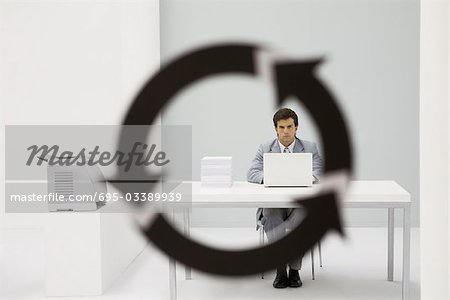 Professional man sitting in office, looking at camera through arrow symbol in foreground