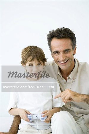 Boy playing video game, father sitting with him, pointing at controller