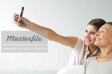 Teenage girl photographing self and grandmother with cell phone, both smiling