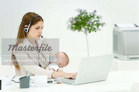 Femme d'affaires au bureau, en tenant le bébé qui dort, à l'aide de casque et ordinateur portable