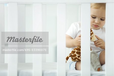 Petit enfant assis dans le lit d'enfant, jouer avec peluche girafe
