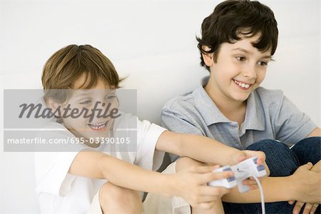 Two boys playing video game together, one holding controller, both smiling
