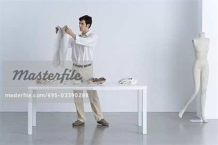 Man standing beside table, holding up sweater