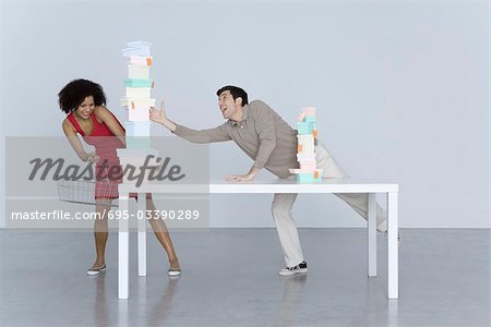 Homme et femme atteignant pour hauteur pile de boîtes, femme tenant le panier d'achat