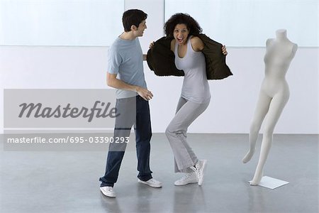 Man helping woman try on jacket, woman smiling at camera