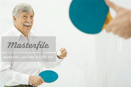 Senior man playing table tennis, hand holding paddle in foreground