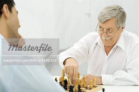 Father playing chess with adult son, smirking