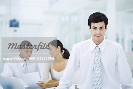 Businessman in office, smiling at camera, employees working in background