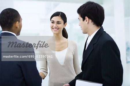 Professional woman standing with two businessman, shaking one man's hand, smiling