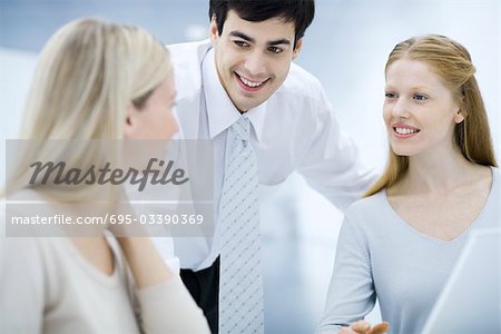 Businessman leaning over, chatting with female colleagues