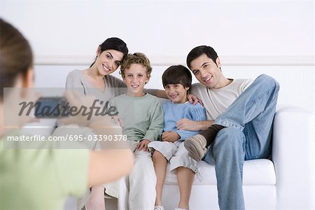 Young girl taking photo of her parents and brothers sitting together on sofa