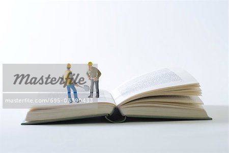 Miniature construction workers standing on open book
