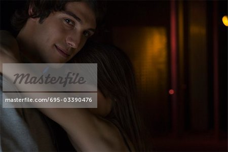 Couple embracing in düster beleuchteten Zimmer, über die Schulter in die Kamera schauen