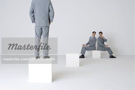 Two identical businessmen whispering over shoulders, third businessman watching