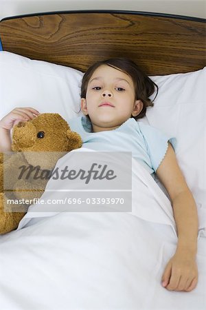 Child lying in bed with teddy bear