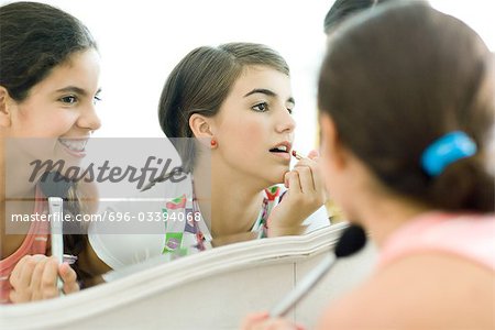 Young female friends looking at mirror, putting on make-up