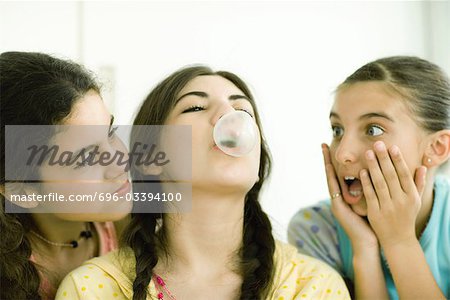 Three young female friends, one blowing bubble while others watch