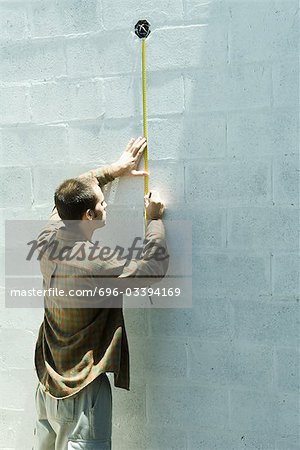 Man using measuring tape on cinder block wall