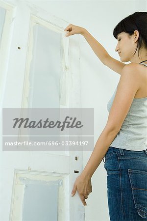 Woman removing masking tape from freshly painted woodwork on door