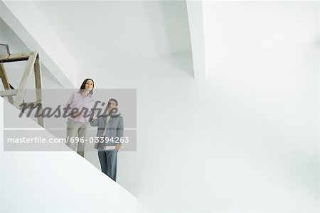 Young woman standing with architect, looking over unfinished interior, low angle view