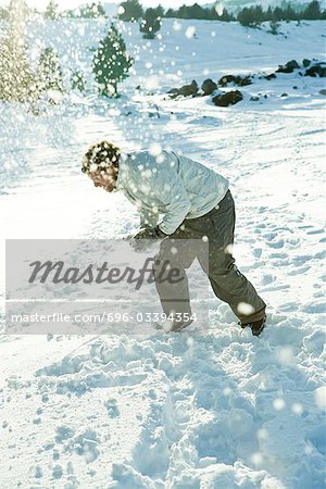 Young man bending over in snow, dodging snowball, full length