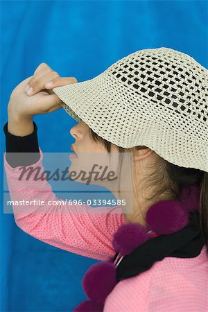 Teenage girl pulling sun hat over eyes, side view, portrait