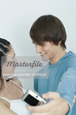 Young couple smiling at each other, man taking photo with digital camera