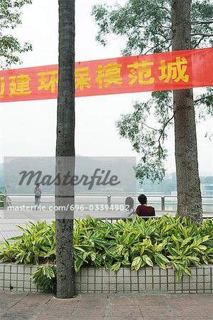 Chine, Province du Guangdong, Guangzhou, couple assis sur un banc près de l'eau, en regardant la vue, vue arrière