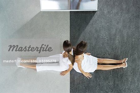 Zwei weibliche teenager sitzen Rücken an Rücken auf schwarz und weiß geteilte Boden, direkt oben aus gesehen