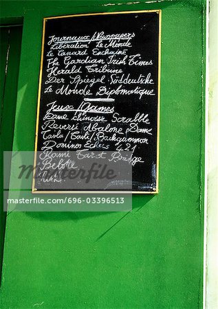 Tableau avec le type en français (liste des journaux et magazines en vente) sur le mur vert.