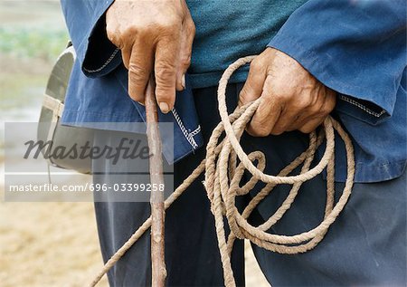 China, peasant holding rope and wood stick, mid-section, close-up