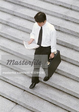 Businessman reading newspaper while walking down steps, high angle view