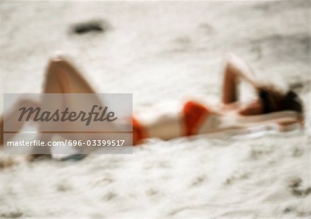 Woman in swimming suit, lying on sand, blurred