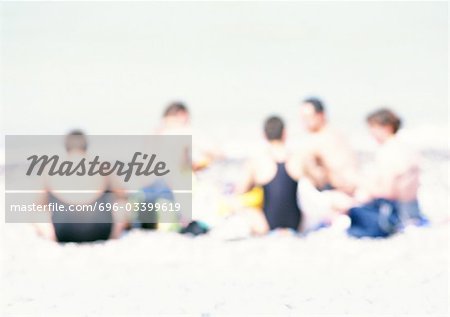 Gruppe von Menschen sitzen auf Sand am Strand, verschwommen